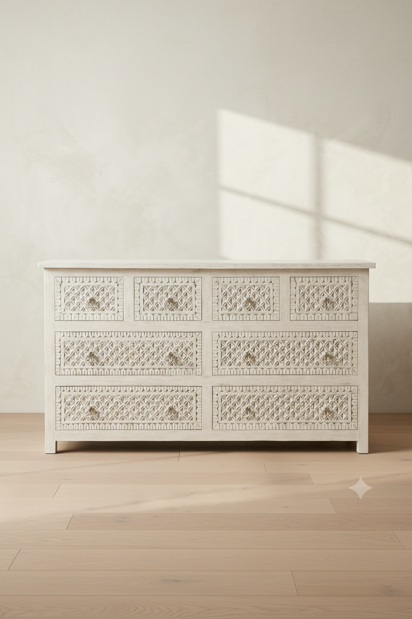 An off-white wooden six-drawer dresser with intricate carved patterns on the drawer fronts, shown in a minimalist room with light wood floors and a textured wall.